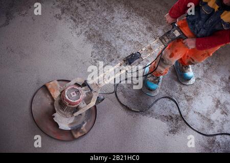 Laborer performing and polishing sand and cement screed floor on the construction site of a new two-level apartment. Sand and cement floor screed Stock Photo