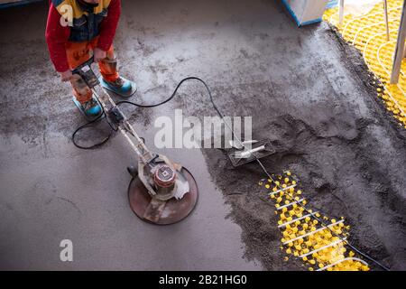 Laborer performing and polishing sand and cement screed floor on the construction site of a new two-level apartment. Sand and cement floor screed Stock Photo