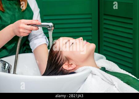 Hairdresser washing woman's hair in sink in beauty salon. Stock Photo