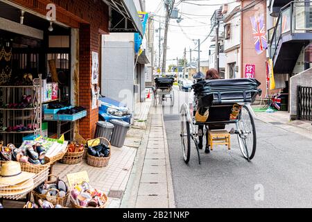 Kyoto, Japan - April 11, 2019: Arashiyama area during spring day with people tourists riding rickshaw carriage tour by stores shops Stock Photo