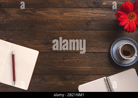 Cozy workplace. Open notebooks, cup of coffee, flower, on wooden background. Flat lay, top view, copy space. Stock Photo