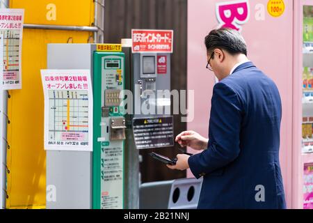 Kyoto, Japan - April 17, 2019: City street in downtown with man buying from parking near vending machine canding local people person salaryman Stock Photo