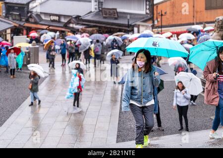 Kyoto, Japan - April 9, 2019: Many people with umbrellas walking up steps in mask during rainy day by street near Kiyomizu-dera temple Stock Photo