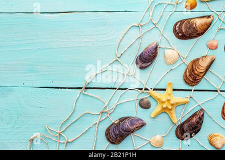 Seashells summer background. Lots of different seashells piled together, mussels, starfish, fishnet (seine) on turquoise wooden boards background, cop Stock Photo