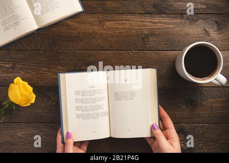 Female hands and opened book, on wooden background. Flat lay, top view, copy space. Stock Photo