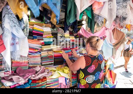 Firenze, Italy - August 30, 2018: Woman buying many scarves colorful vibrant colors hanging on display in shopping street market in Florence, Tuscany Stock Photo