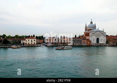 Houses, businesses, boats, bridges and the Basilica or Chiesa Del Santissimo Redentore as seen from the canal Giudecca. Early morning light. Stock Photo