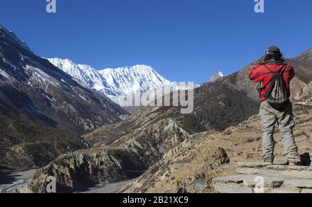 Local Nepal Man admiring landscape views of Distant Snowcapped Peaks on Annapurna Circuit Hiking and Trekking Trail in Himalaya Mountains Stock Photo