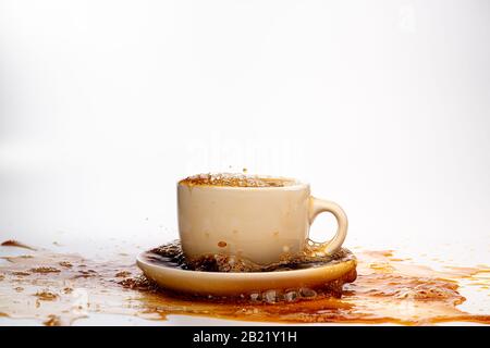 Coffee pouring into a white cup isolated against a plain white background, splashing in all directions creating a mess on the white surface Stock Photo