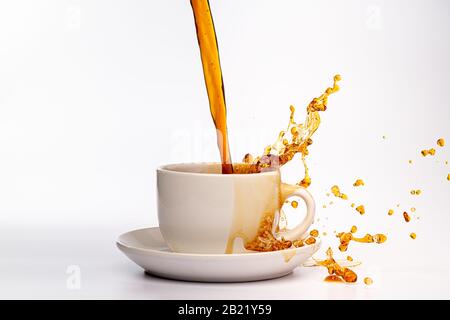 Coffee pouring into a white cup isolated against a plain white background, splashing in all directions creating a mess on the white surface Stock Photo