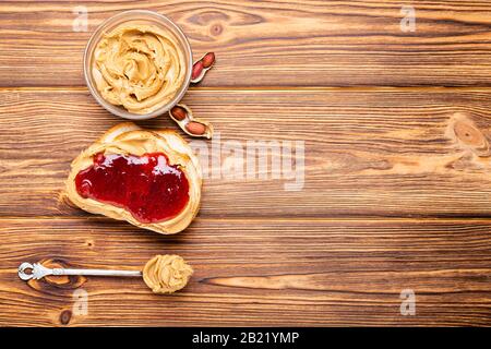 Toast sandwich with peanut butter. Spoon and jar of peanut butter, jam and peanuts for cooking breakfast on a brown wooden background. Creamy peanut Stock Photo