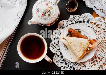 A Beautiful Version Of Breakfast With A White Porcelain Cup And A Painted  Teapot In The Background, Ready-made Pancakes On A Saucer. Table Setting  For The Russian Holiday Maslenitsa Stock Photo, Picture