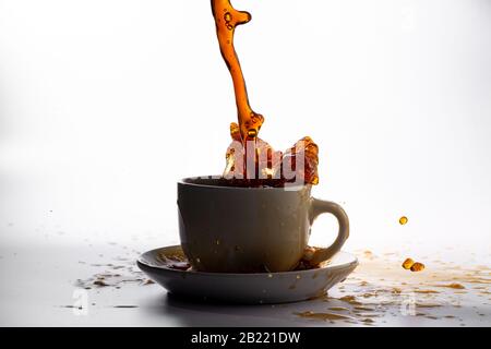 Coffee pouring into a white cup isolated against a plain white background with backlighting and coffee darker, splashing in all directions creating a Stock Photo