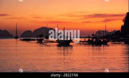 Traditional philippine boat bangka at sunset time. Beautiful sunset with silhouettes of philippine boats in El Nido, Palawan island, Philippines. Stock Photo
