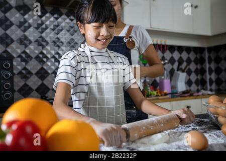 Happy Family and their little daughter preparing a pizza, knead the dough and puts ingredients on kitchen table Stock Photo