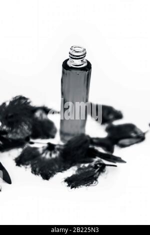 Red or pink colored flowers isolated on white along with their essential oil in a transparent glass bottle along with them. Stock Photo