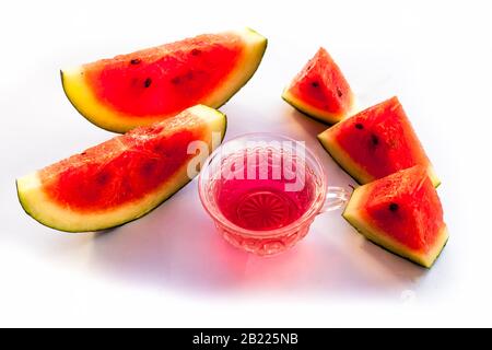 Detoxifying Watermelon seed's tea in a transparent glass cup along with watermelon pieces in triangle shape isolated on white. Stock Photo