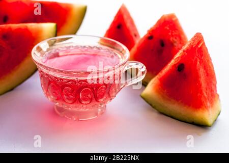 Detoxifying Watermelon seed's tea in a transparent glass cup along with watermelon pieces in triangle shape isolated on white. Stock Photo