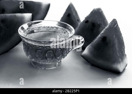 Detoxifying Watermelon seed's tea in a transparent glass cup along with watermelon pieces in triangle shape isolated on white. Stock Photo