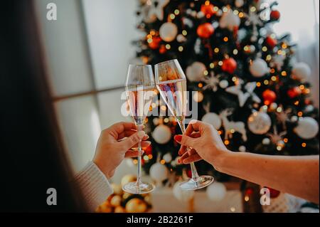 two cheers glasses with champagne against the background of the Christmas tree in female hands Stock Photo