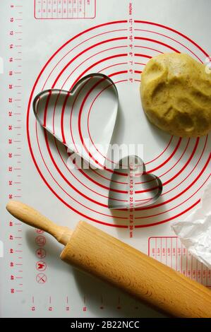 baking scenery with heart shaped cookie cutter, rolling pin for dough, silicone baking mat. Romantic food, photo for recipe book. Stock Photo