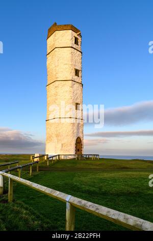 Exterior of old sunlit Flamborough Head Lighthouse (historic tall white chalk octagonal beacon tower) & deep blue sky - Yorkshire Coast, England, UK. Stock Photo