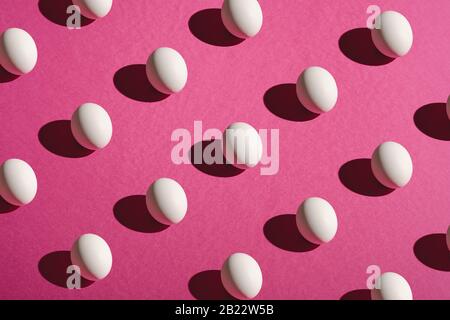 White eggs pattern on pink purple colors plain minimal background, angle view, happy Easter day Stock Photo
