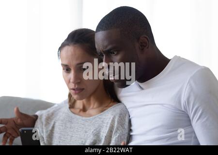 Shocked African American man and woman looking at phone Stock Photo