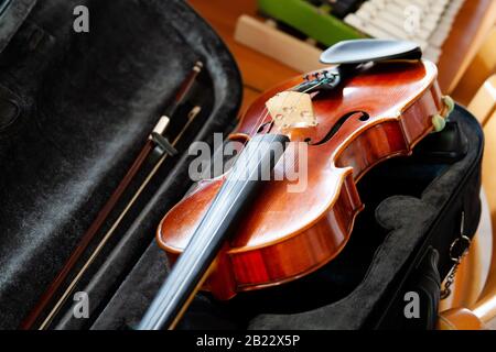 Violin, fiddle with a bow laying in an open black case on the table, small xylophone in the back. Simple classical musical string instruments group Stock Photo