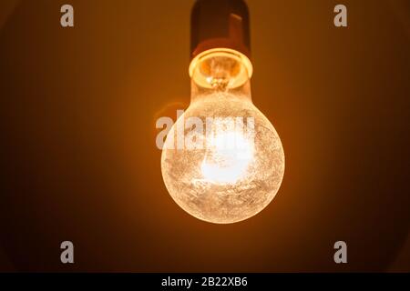 Bright overexposed yellow old dirty lightbulb abstract. Circular lens flare, bright new idea or creepy spooky warm lighting concept, closeup, power Stock Photo