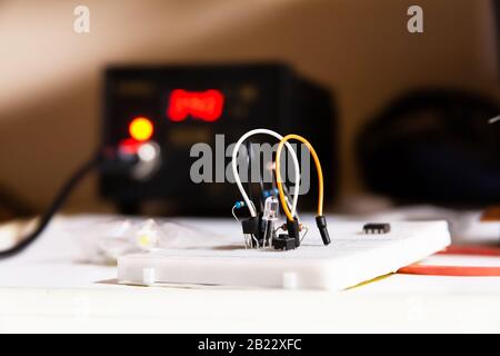 Simple electric circuit, white breadboard with electrical components, wires, diode, resistors, soldering station in the background, project Stock Photo