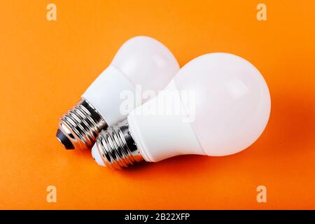 Two small bright white energy saving bulbs. Pair of modern eco lightbulbs laying isolated on orange background. Power saving, ecologic lifestyle Stock Photo