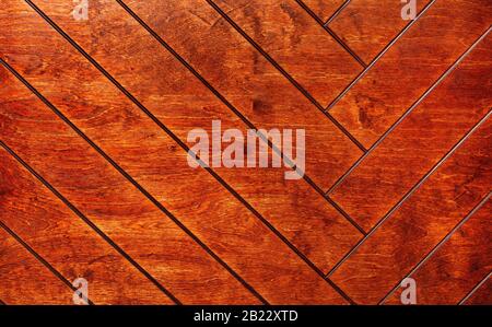 Old wooden boards painted with orange paint form a herringbone pattern, wood texture. Stock Photo