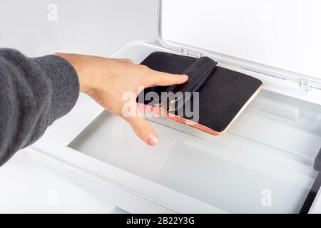 Man photocopying, scanning an old book on an open photocopier home printer Top view, hand placing a small book spread on copier glass surface Archivin Stock Photo
