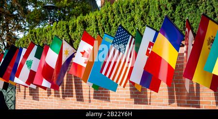Row of many different flags hanging from a brick wall during the day. Representing of countries Multi cultural event, mix of culture patriotic symbols Stock Photo