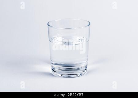 One simple half full half empty glass of fresh crystal clear clean drinking water, solo object isolated on light blue background. Hydration and health Stock Photo