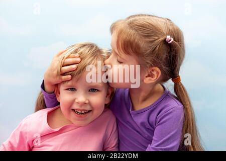 Two little girls, preschoolers, young sisters siblings smliling, laughing. Children kiss on the head concept. Care and love in family, childhood Stock Photo