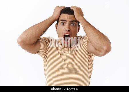 Scared, horrified young strong man in panic feeling afraid to death, holding hands on head, screaming and staring alarmed camera, have phobia Stock Photo