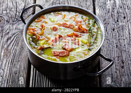 German pea stew erbseneintopf with bacon, pork meat, carrot, potato with thyme - winter hearty dish served on a pot on an old barn wooden table, horiz Stock Photo