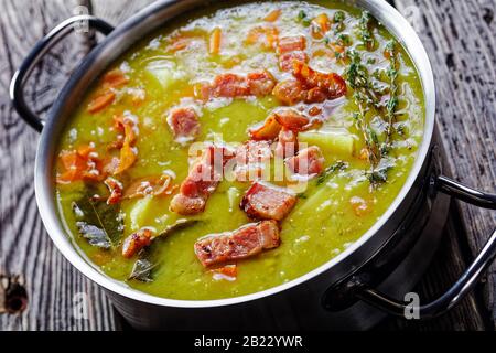 German pea stew erbsensuppe with bacon, pork meat, carrot, potato with thyme - winter hearty dish served on a pot on an old barn wooden table, horizon Stock Photo