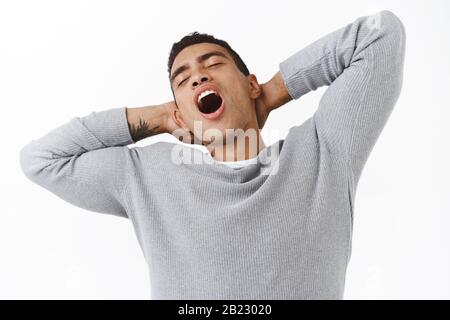 Close-up lazy handsome young hispanic guy with athletic body, stretching and holding hands behind head, yawning with closed eyes tired, feeling sleepy Stock Photo