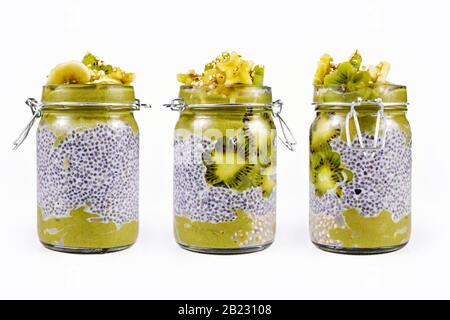 Layered green fruit smoothie in glass with chia seed pudding topped with star shaped banana and kiwi slices isolated on white background, view from di Stock Photo