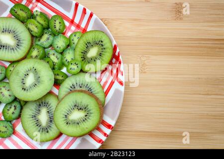 Sliced kiwi fruit and kiwi berries arranged on a rustic plate on a wooden cutting board. Stock Photo