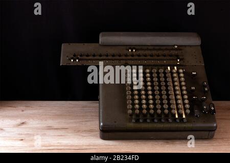 Old counting mechanism, dusty vintage arithmometer standing on a wooden board against black fabric Stock Photo