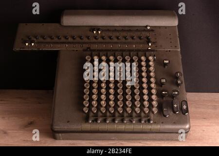 Old counting mechanism, dusty vintage arithmometer standing on a wooden board against black fabric Stock Photo