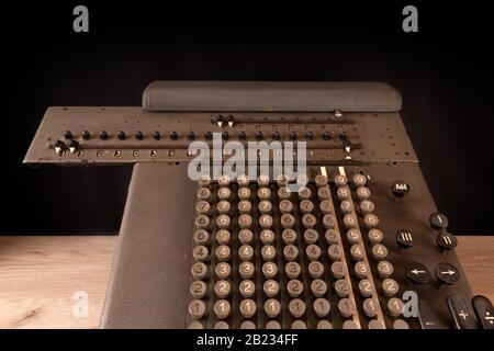 Old counting mechanism, dusty vintage arithmometer standing on a wooden board against black fabric Stock Photo