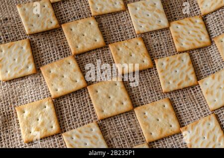 Geometric pattern of salted crackers. Square treats on burlap background. Repeating loop ornament. Selective focus. Close-up. Stock Photo