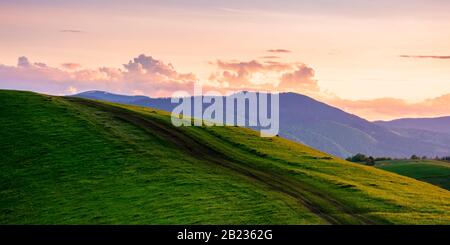 rural landscape in mountains at dusk. amazing view of carpathian countryside with dirt road through rolling hills. glowing purple clouds on the sky. c Stock Photo