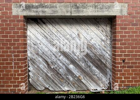 a vintage retro diagonal faded wooded shipping and receiving loading dock door on an old red brick building in an alley Stock Photo