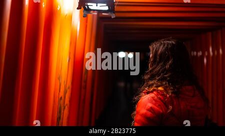 Kyoto, Japan with back of woman walking through red Fushimi Inari shrine torii gates in park at night with illumination lanterns by path Stock Photo